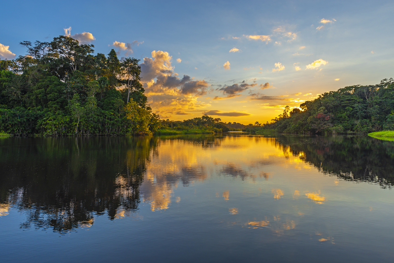 A sunset over rainforest reflected in a calm river.