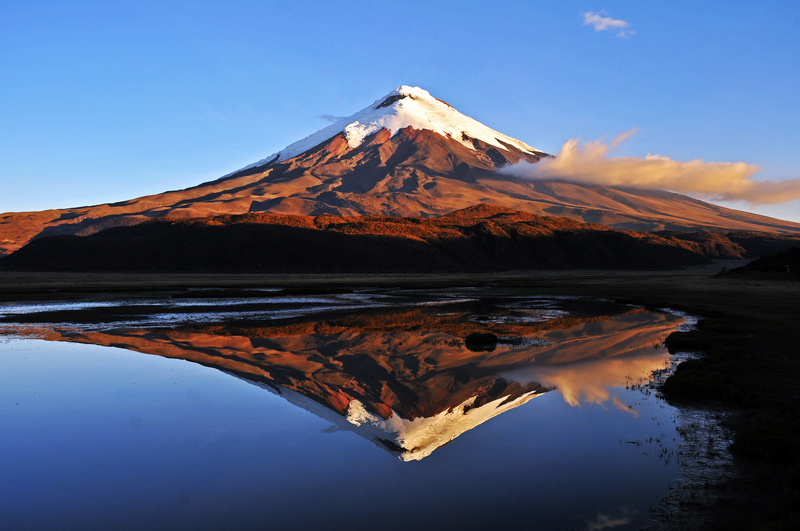 Image of snowcapped mountain illuminated by sun and reflected in still lake.