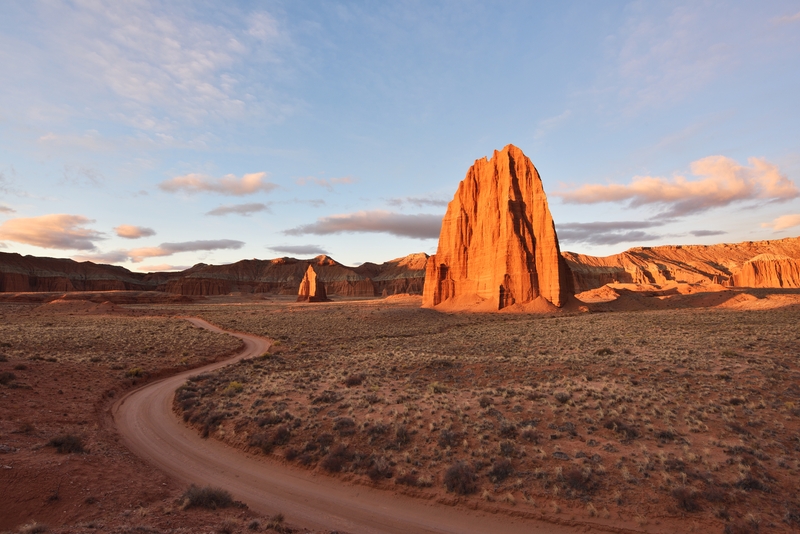 Image of desert valley with a couple towering red rock formations illuminated by the sun.