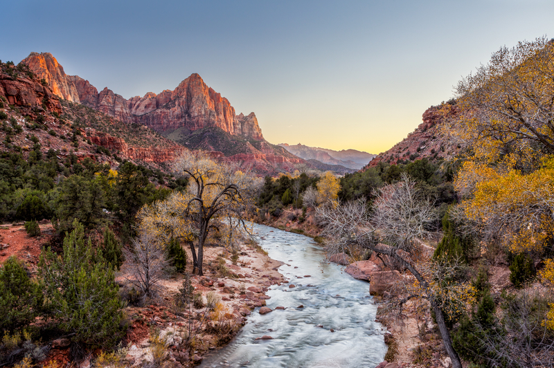 Image of a river rushing through a valley with fall trees and red mountains in the distance.