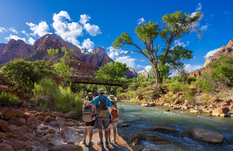 A family stands facing a river flowing through a lush valley with their arms wrapped around each other.