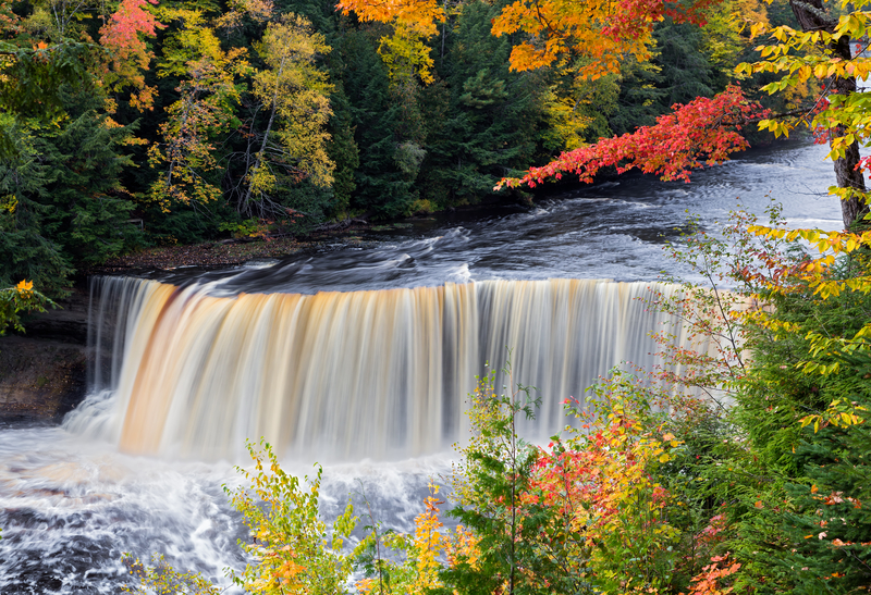 Image of wide rushing waterfalls in a colorful autumnal forest.