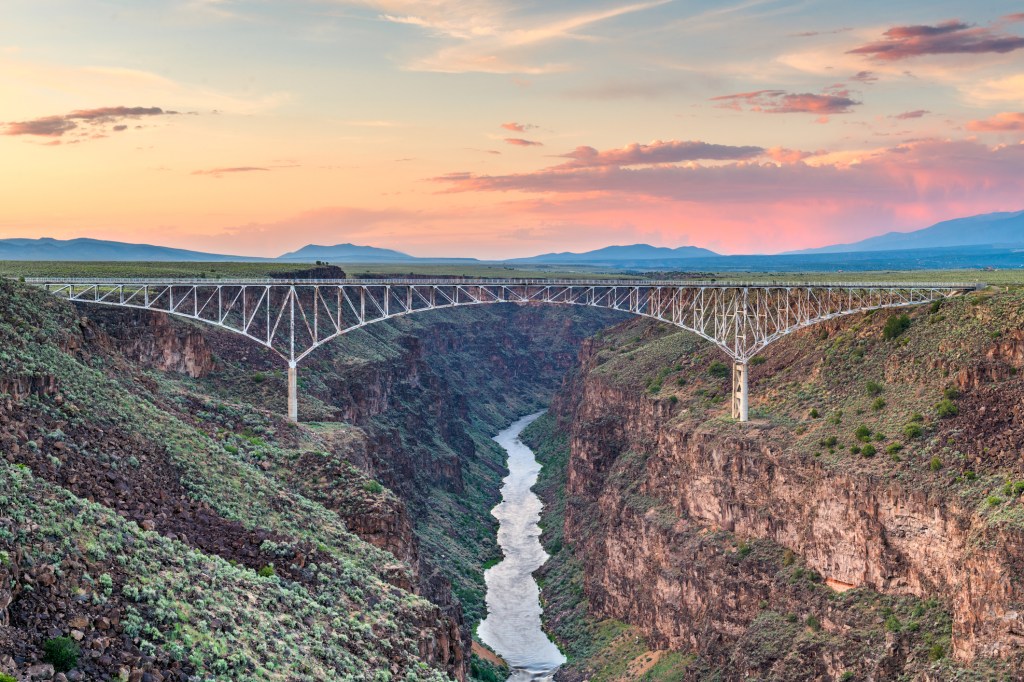 A bridge across a deep river gorge under pink sunset