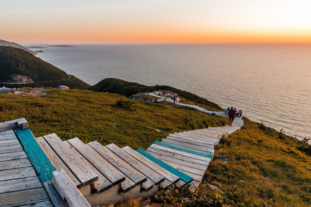 A boardwalk trail of wooden steps leading down a hill overlooking the ocean at sunset.