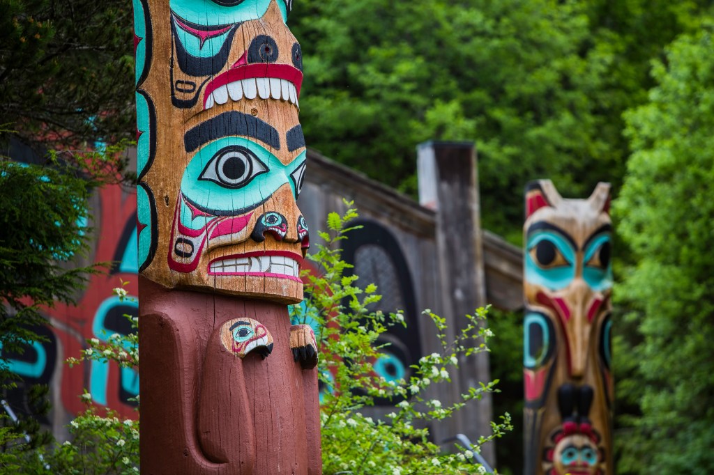 Image of colorful totem poles against background of lush green trees