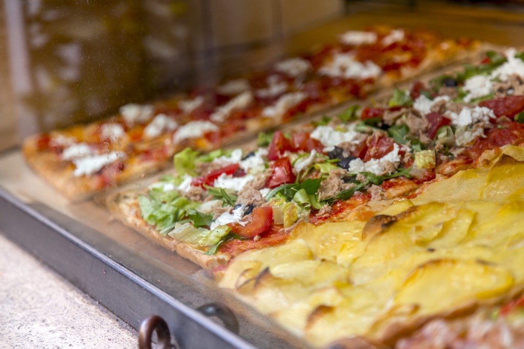 Three rectangular pizzas with various toppings displayed in a window