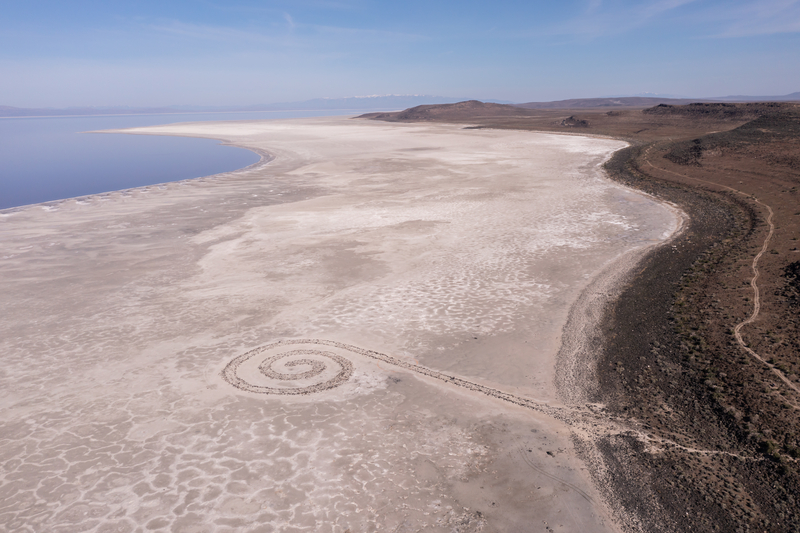 Aerial image of arid land next to lakeshore with a spiral shape formed out of rocks.