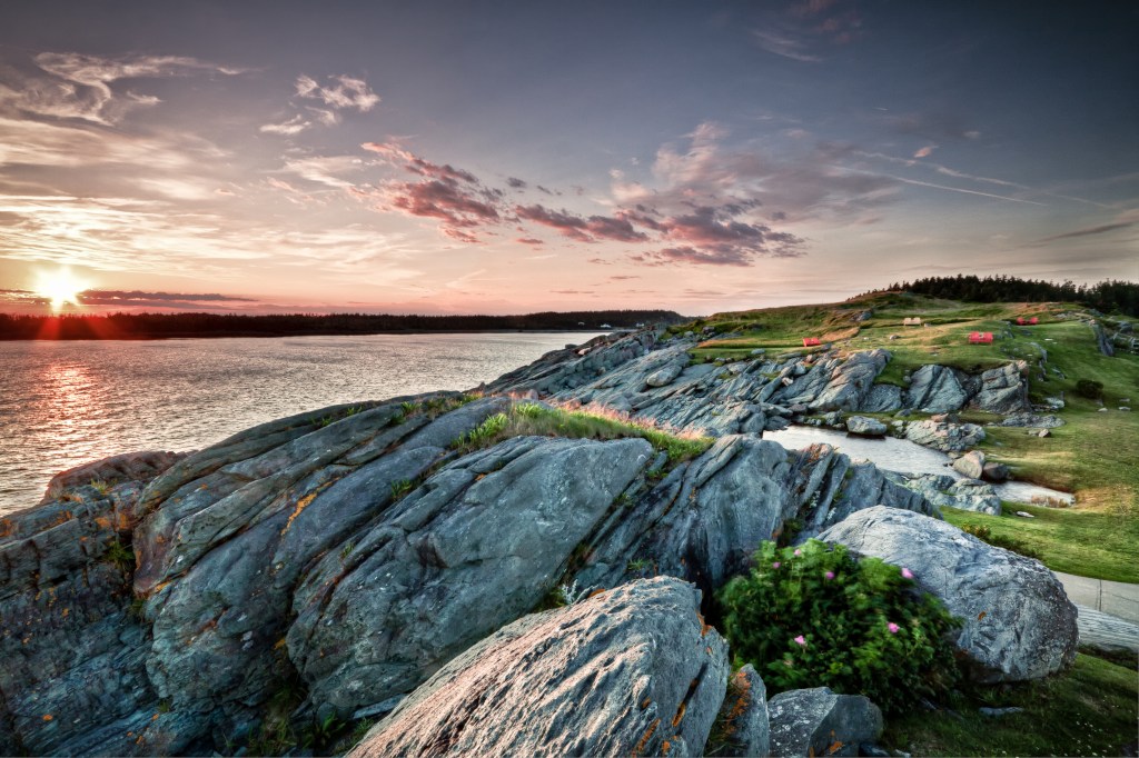 Image of green rocky cliffs overlooking ocean under orange and purple sunset.