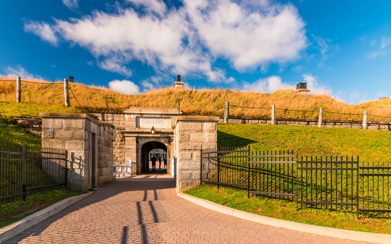 A path leading through a stone tunnel lined with green grass under blue sky.