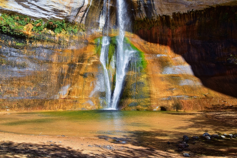 Image of thin waterfalls cascading over colorful orange and green rock formations.