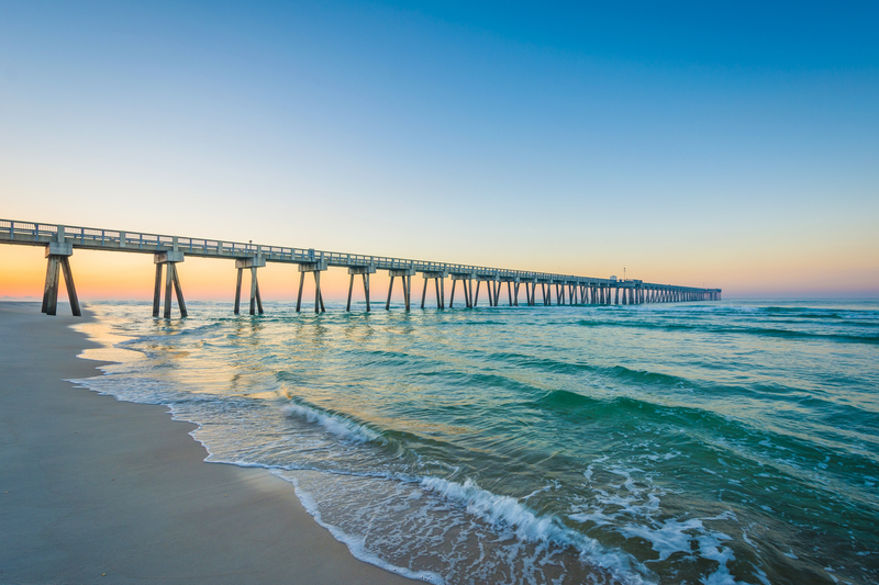 Image of pier above turquoise ocean on beach at sunset.