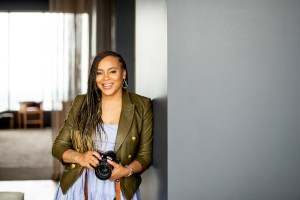 Photo of author TaKiyah Wallace-McMillian standing in a doorway holding a camera. She is smiling.