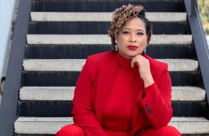 Photo of author Zenda Walker. She is sitting on a staircase in a red power suit and looking into the camera with her chin on her hand.