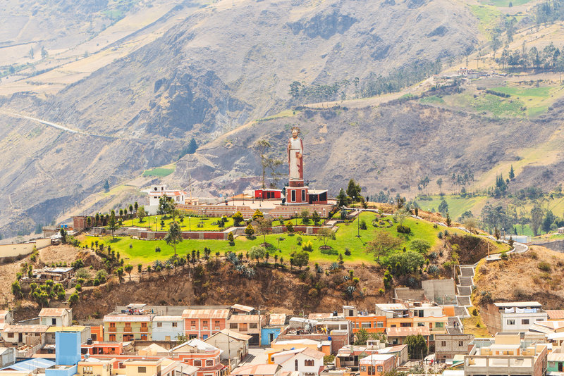 Image of a green hill in the middle of a colorful town with a towering statue at the top.