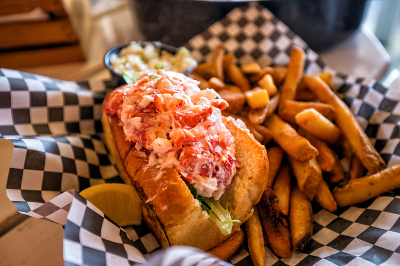 Image of lobster rolls with fries and a lemon slice in a basket lined with black and white checkered paper.