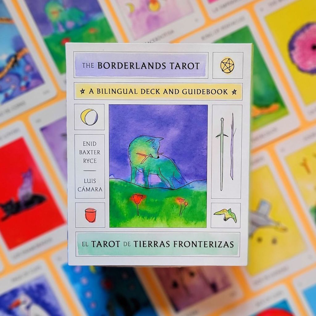 Photo of “The Borderlands Tarot / El Tarot de Tierras Fronterizas” laid above face-up cards from the deck against an orange background