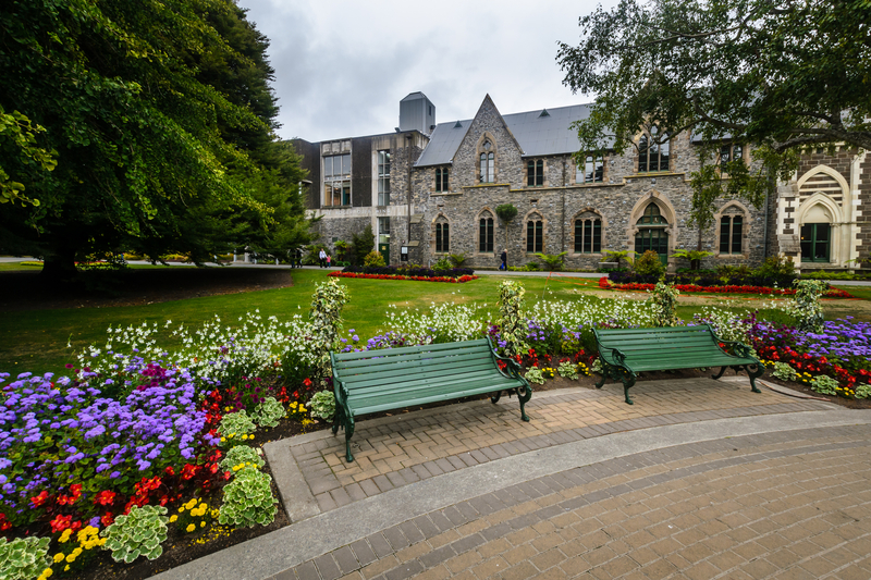 Image of pretty grey stone building with flowers and garden and benches in the foreground.