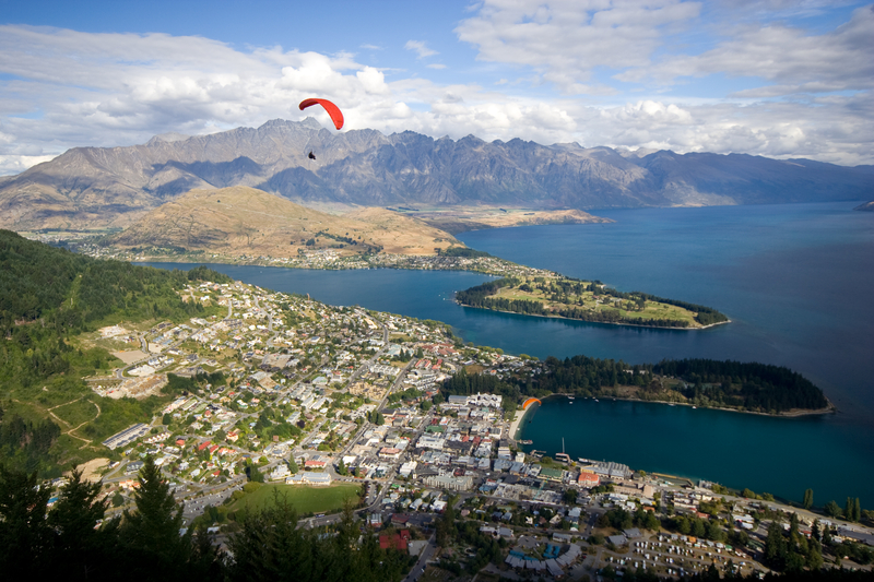 A paraglider soars over a city next to the ocean.