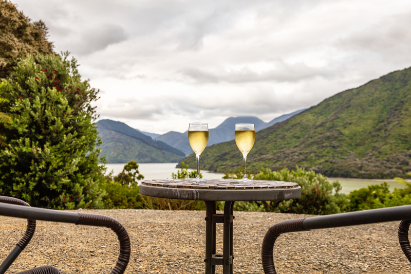 Image of small table and chairs with two glasses of white wine and lush green hilly landscape in the distance.