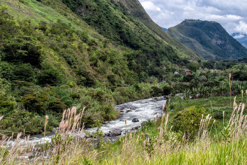 Image of the bank of a river running alongside green mountain slopes.