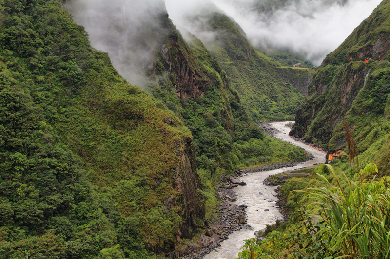 A river winds through a lush green mountain valley with wispy white clouds.