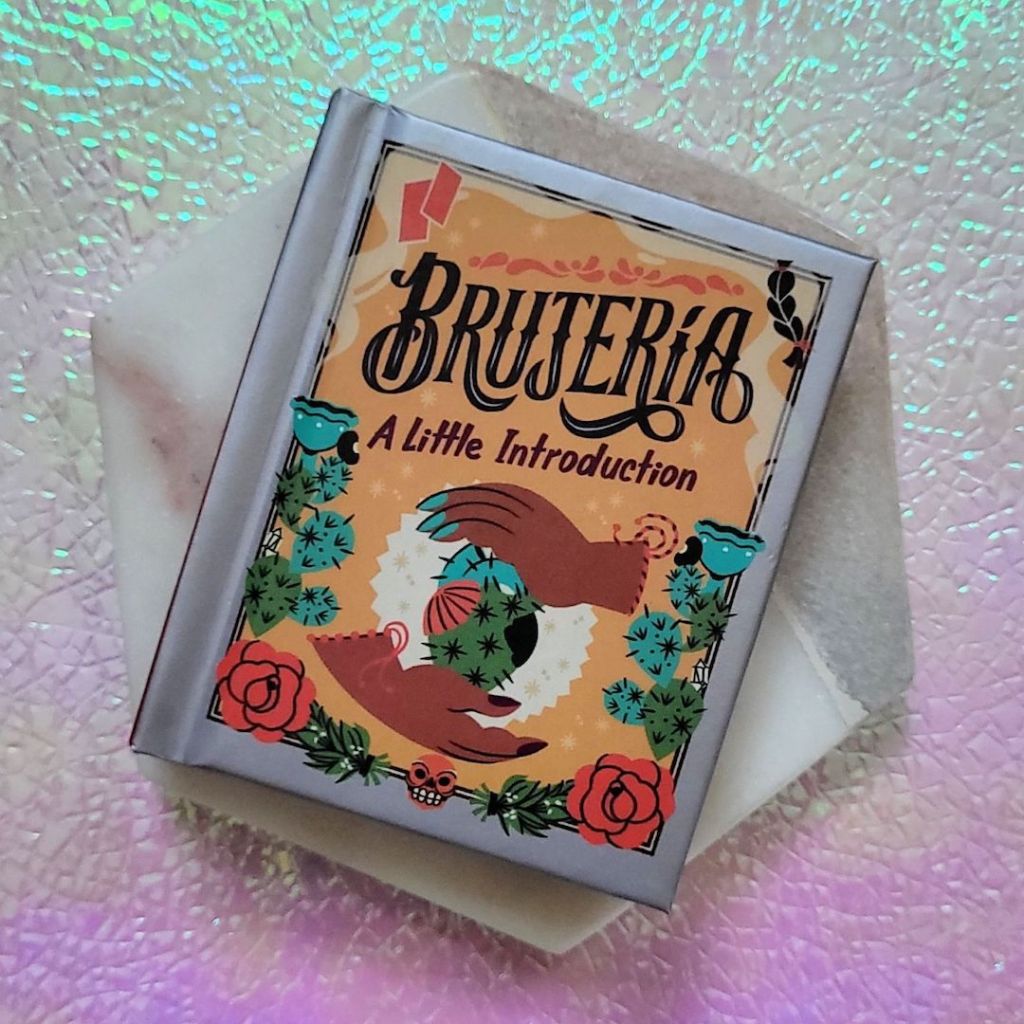 Photo of “Brujería: A Little Introduction” laid on a marble hexagon above a pink and green iridescent background