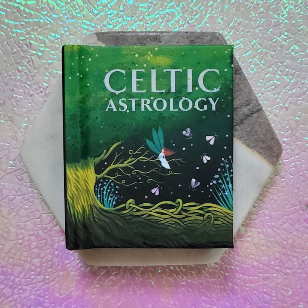 Photo of “Celtic Astrology” laid on a marble hexagon above a pink and green iridescent background