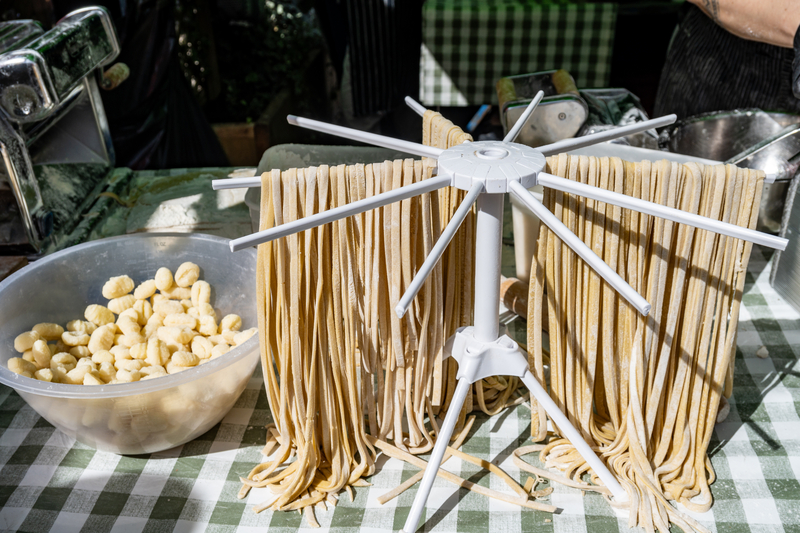 Fresh tagliatelle pasta hanging to dry on a rack next to a bowl of fresh gnocchi on a checkered tablecloth