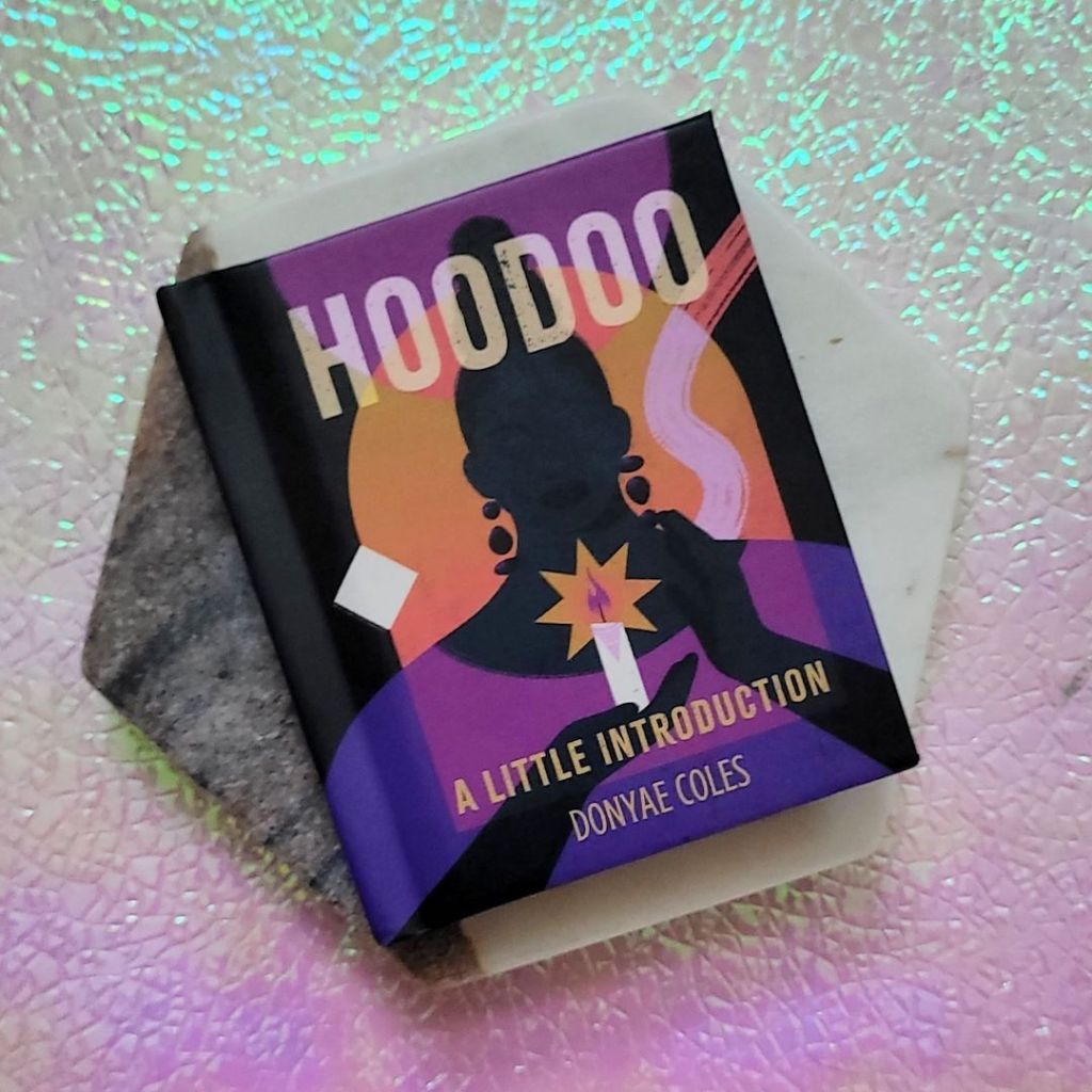 Photo of “Hoodoo: A Little Introduction” laid on a marble hexagon above a pink and green iridescent background