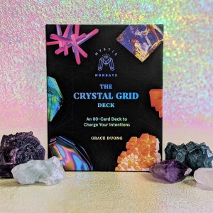 Photo of "Mystic Mondays: The Crystal Grid Deck" standing among various crystals in front of a pink and green iridescent background