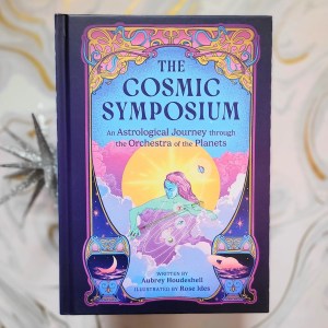 Photo of “The Cosmic Symposium: An Astrological Journey through the Orchestra of the Planets” laid above a white and gold marbled backdrop